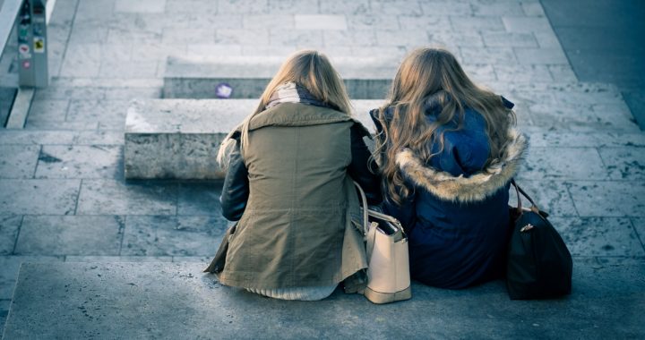 two girls sitting on a concrete bench facing away