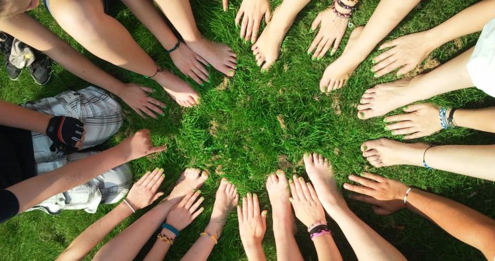 a group of people sitting outside on the grass with their feet and hands in a circle